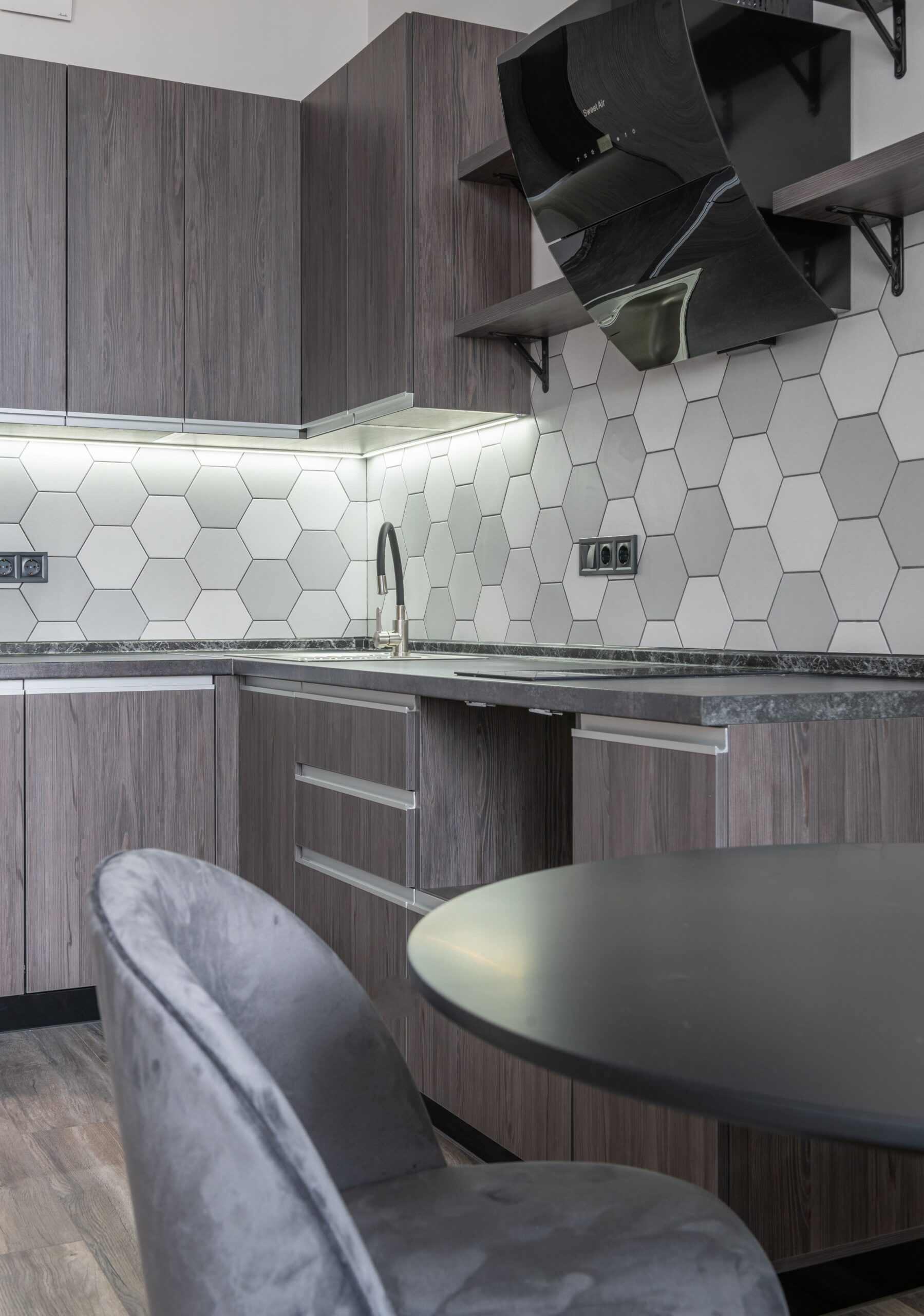 Modern kitchen with hood against cupboards above cabinets in light house with table and chair