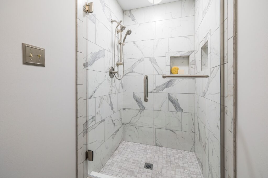 Elegant bathroom with white marble tiles and glass door, showcasing modern interior design.